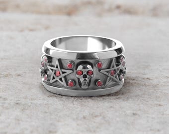 May include: A silver ring with a detailed design featuring a skull and pentagrams. The ring has red gemstone accents and a polished finish. The ring is a gothic or alternative style.