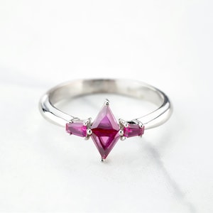 May include: A silver ring with a pink gemstone in the center and two smaller pink gemstones on either side.