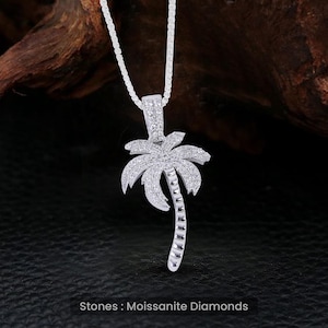 Könnte beinhalten: Eine silberne Halskette mit einem Palmen-Anhänger, der mit klaren Steinen besetzt ist. Der Anhänger ist aus Silber und hat ein detailliertes Design. Die Steine sind in einer Pavé-Fassung gefasst und funkeln hell. Steine: Moissanite-Diamanten.