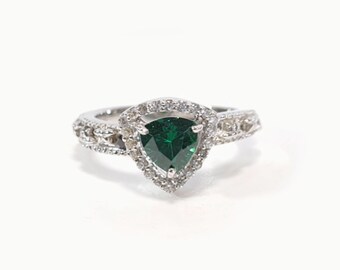 May include: A silver ring with a green triangular gemstone surrounded by smaller white gemstones. The band of the ring is decorated with a delicate design.