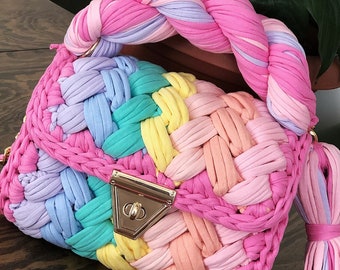 May include: A colorful crocheted handbag with a braided handle and a chain strap. The bag is made of multiple colors of yarn, including pink, blue, yellow, and green.