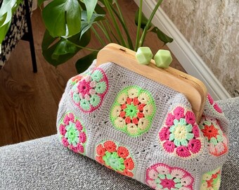 Puede incluir: Un bolso de crochet con marco de madera y diseños florales coloridos en tonos rosa, verde y amarillo.