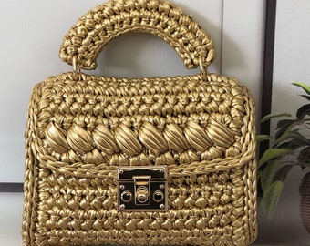 May include: A gold woven handbag with a top handle and a chain strap. The bag has a gold metal clasp.