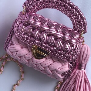 May include: A pink woven handbag with a gold chain strap and a pink tassel. The bag has a woven top and a solid pink bottom.