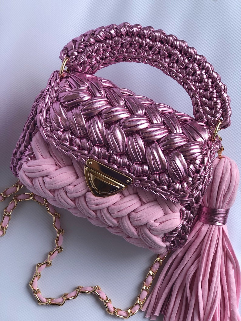 May include: A pink woven handbag with a gold chain strap and a pink tassel. The bag has a woven top and a solid pink bottom.