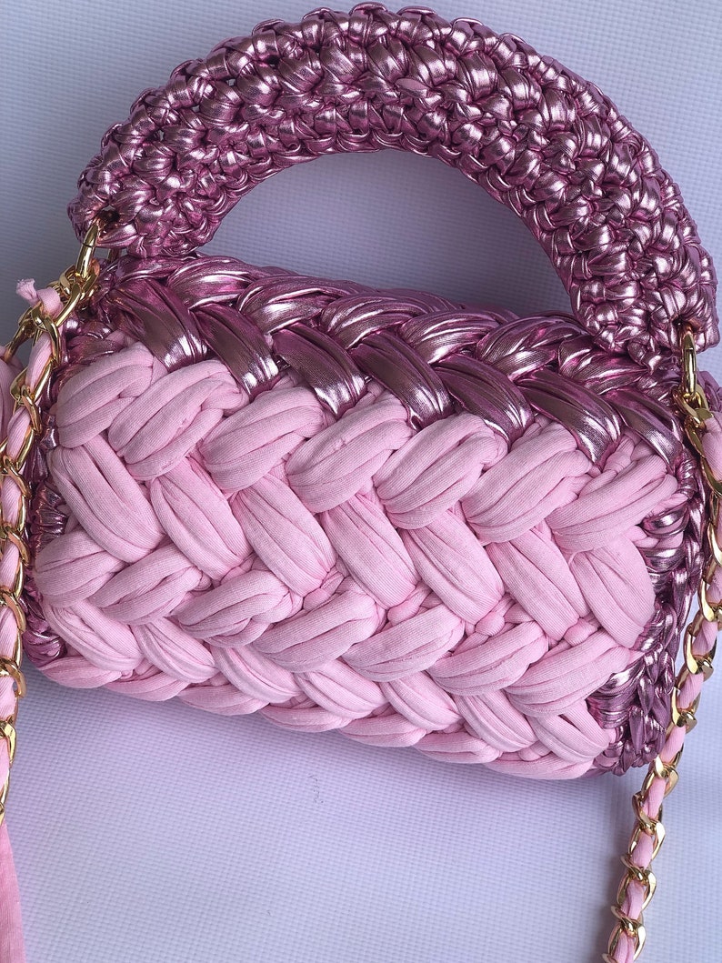 May include: A pink woven handbag with a metallic pink top and a gold chain strap.