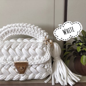 Peut inclure: Sac &agrave; main en crochet blanc avec une fermeture dor&eacute;e et un long pompon. Le sac a un design tress&eacute; et une poign&eacute;e sup&eacute;rieure.