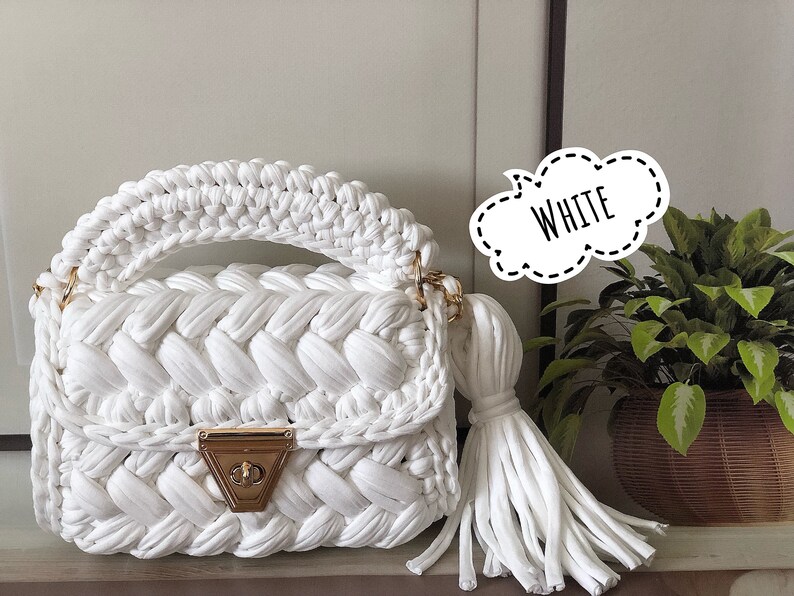 Peut inclure: Sac &agrave; main en crochet blanc avec une fermeture dor&eacute;e et un long pompon. Le sac a un design tress&eacute; et une poign&eacute;e sup&eacute;rieure.
