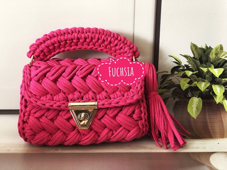 Peut inclure: Un sac &agrave; main en crochet fuchsia vif avec un fermoir dor&eacute; et un pompon. Le sac a une texture tiss&eacute;e et est &eacute;tiquet&eacute; "Fuchsia".