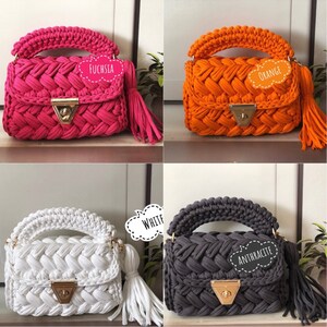 Peut inclure: Quatre sacs &agrave; main en crochet de diff&eacute;rentes couleurs&nbsp;: fuchsia, orange, blanc et anthracite. Chaque sac a un design tress&eacute;, un fermoir dor&eacute; et un pompon.