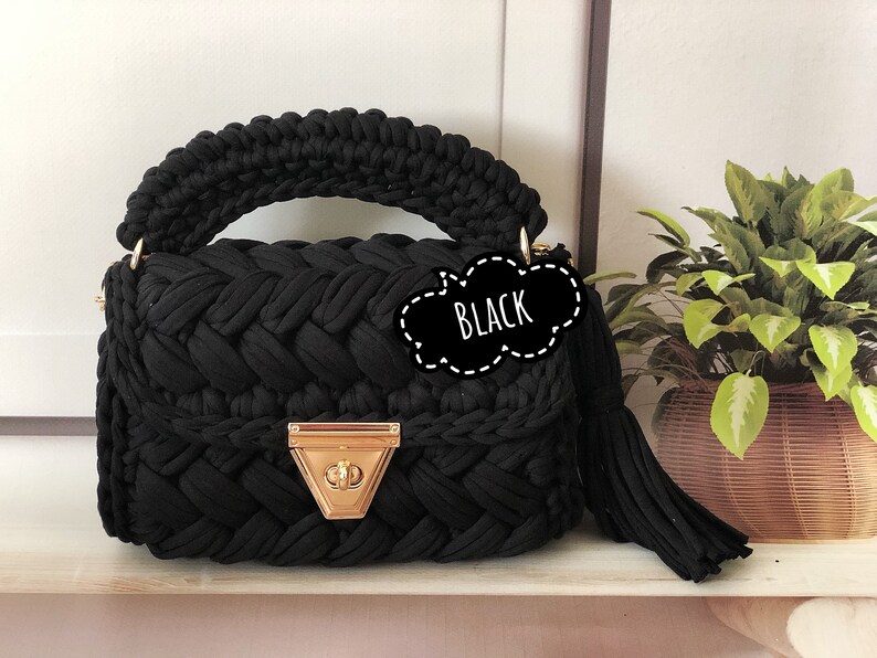 Peut inclure: Sac &agrave; main en crochet noir avec un fermoir dor&eacute; et un pompon noir. Le sac a un design tress&eacute; et une poign&eacute;e sup&eacute;rieure.