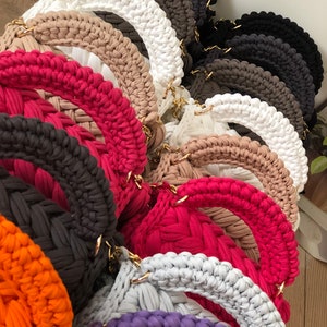 Peut inclure: Une collection de sacs en crochet de diff&eacute;rentes couleurs, notamment blanc, beige, rouge, orange, violet et gris. Les sacs sont de forme ronde et sont faits d'un fil &eacute;pais et textur&eacute;.