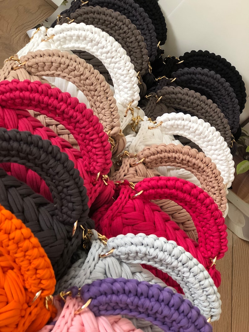 Peut inclure: Une collection de sacs en crochet de diff&eacute;rentes couleurs, notamment blanc, beige, rouge, orange, violet et gris. Les sacs sont de forme ronde et sont faits d'un fil &eacute;pais et textur&eacute;.