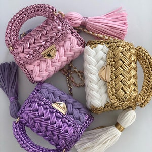 May include: Three small crocheted handbags with gold chain straps and tassels. The handbags are pink, white and gold, and purple.