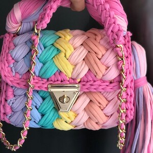 May include: A small, colorful crocheted handbag with a gold chain strap and a gold clasp. The bag is made of multiple colors of yarn, including pink, purple, blue, green, and yellow.