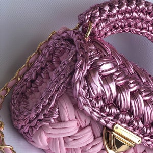 May include: A pink woven handbag with a gold chain strap and a gold clasp. The bag has a unique woven design and a top handle.