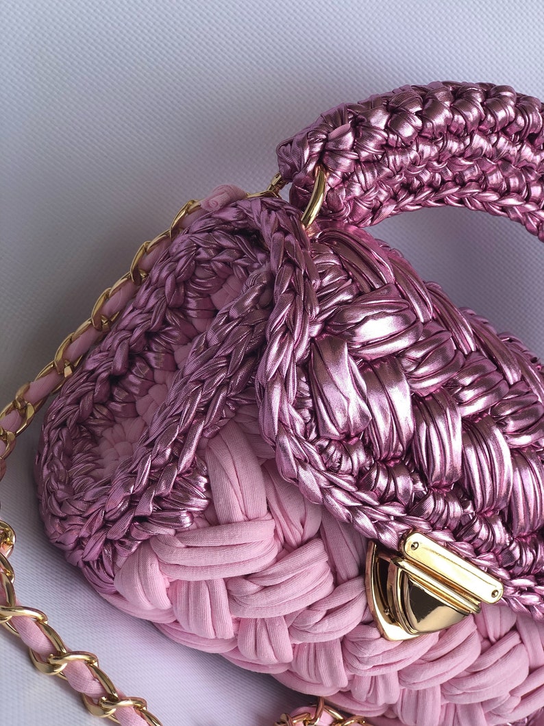 May include: A pink woven handbag with a gold chain strap and a gold clasp. The bag has a unique woven design and a top handle.