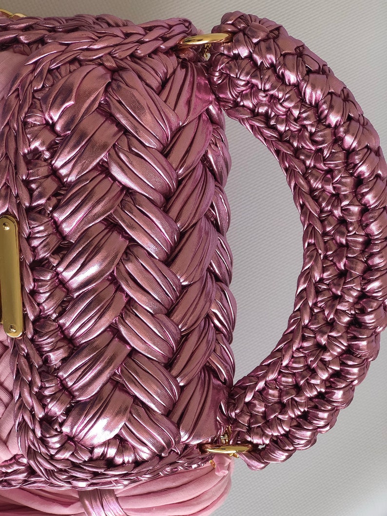 May include: A pink woven handbag with a braided handle and gold hardware.