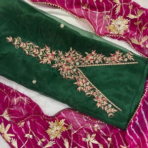 May include: A dark green fabric with intricate floral embroidery in gold and red. The design is complemented by a vibrant pink fabric with gold accents. The ensemble suggests a traditional garment, possibly a dress or a set.