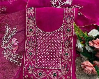May include: A vibrant fuchsia-colored salwar kameez set. The top features intricate embroidery with white, green, and gold accents around the neckline and borders. A matching dupatta with floral embroidery and a solid bottom complete the ensemble. The fabric appears to be a lightweight, sheer material.