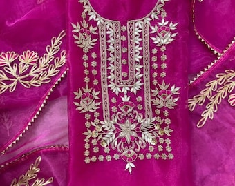 May include: A vibrant fuchsia-colored outfit with intricate gold embroidery. The design features floral and leaf patterns, with embellishments on the neckline and bodice. The sheer fabric is complemented by matching gold trim.