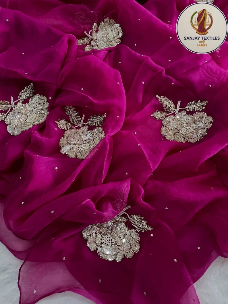 May include: A vibrant magenta fabric with intricate silver floral embroidery and scattered silver sequins. The fabric is draped, showcasing its flowing texture and the detailed craftsmanship of the embellishments.