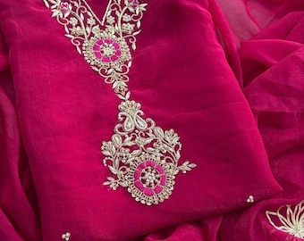 May include: A vibrant fuchsia-colored garment with intricate gold and pink embroidery. The embroidery adorns the neckline and a central design element. The fabric appears to be a lightweight, flowing material, possibly silk or chiffon.