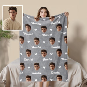 May include: A grey fleece blanket with a repeating pattern of a person's face and the name "Daniel" in white text. White hearts are scattered throughout the pattern.