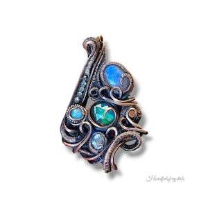 May include: A handcrafted pendant featuring a complex wire-wrapped design. The pendant incorporates various gemstones, including a large central emerald-cut stone, opals, and smaller blue-green crystals. The wire is a copper color, and the overall design is intricate and artistic.