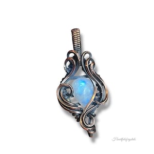 May include: A handcrafted pendant featuring a luminous, blue-hued gemstone encased in an ornate, swirling metal frame. The pendant's design incorporates intricate wirework, creating a unique and artistic piece of jewelry. The pendant is suspended from a textured bail.