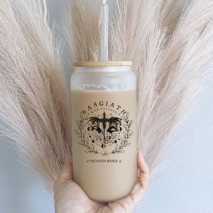 May include: A clear glass tumbler with a bamboo lid and a black and white graphic of a dragon with the text "Basgiath *War College* Dragon Rider" printed on the side.