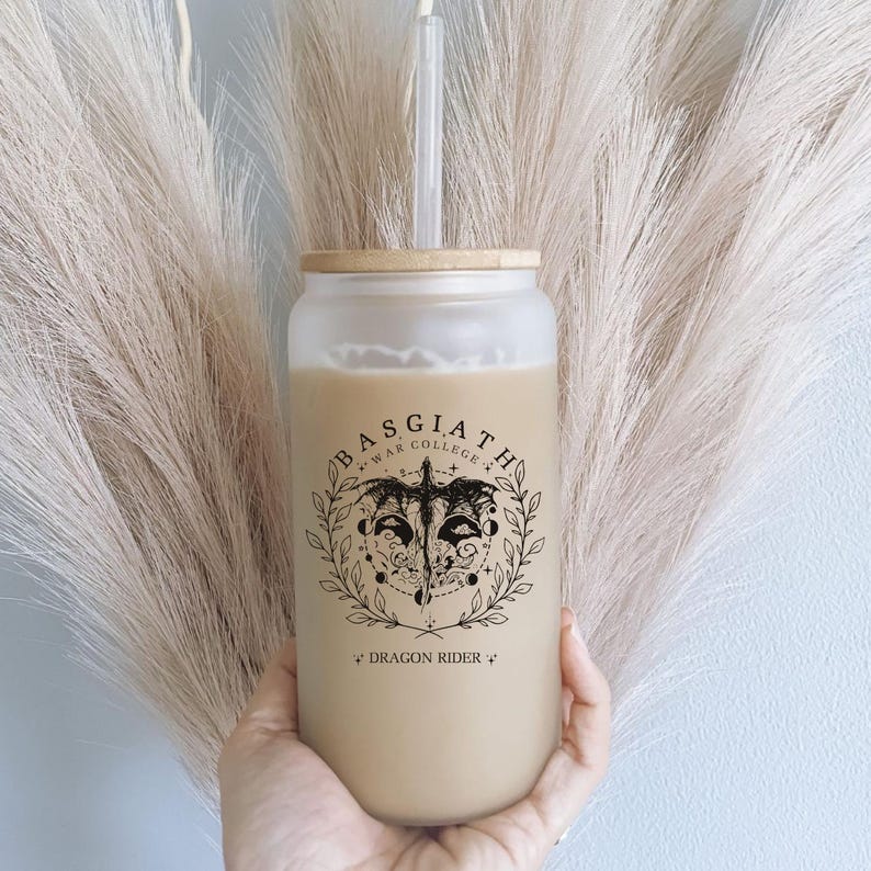 May include: A clear glass tumbler with a bamboo lid and a black and white graphic of a dragon with the text "Basgiath *War College* Dragon Rider" printed on the side.