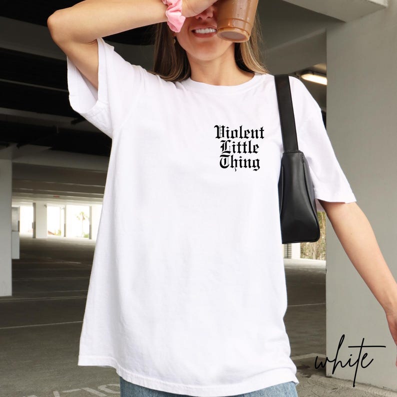 May include: White t-shirt with the text "Violent Little Thing" in a gothic font. The shirt is a basic crew neck style. The word "white" is written in a script font in the bottom right corner.