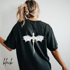 May include: Black t-shirt featuring a white dragon design on the back. The dragon has outstretched wings and a long tail. The word "black" is written in a script font at the bottom left of the shirt.