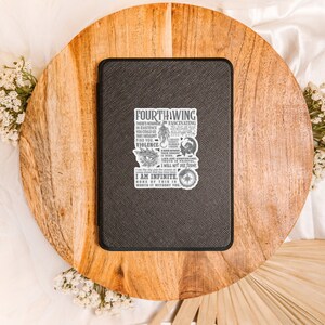 May include: A black leather notebook with a white sticker featuring a quote from the book "Fourth Wing" by Rebecca Yarros. The quote reads: "There's none fascinating in existence you could go... I am infinite. None of this is worth it without the..."