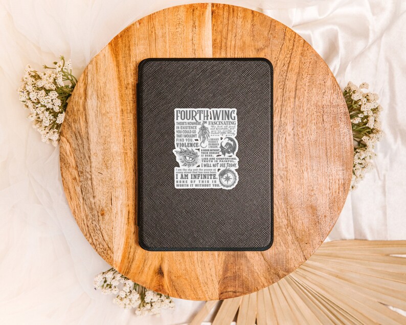 May include: A black leather notebook with a white sticker featuring a quote from the book "Fourth Wing" by Rebecca Yarros. The quote reads: "There's none fascinating in existence you could go... I am infinite. None of this is worth it without the..."