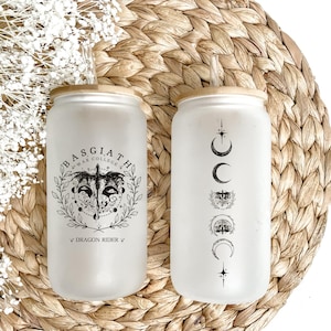 May include: Two frosted glass tumblers with bamboo lids and reusable glass straws. One tumbler features a black and white illustration of a dragon with the text "Basgiath War College *Dragon Rider*" and the other tumbler features a black and white illustration of a crescent moon, stars, and a wolf's head.