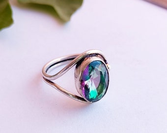May include: A silver ring with a large oval-shaped gemstone. The gemstone is iridescent and displays shades of green, blue, and purple.