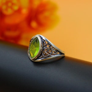 Può includere: Un anello d'argento con una pietra preziosa verde incastonata in un design a nodo celtico.