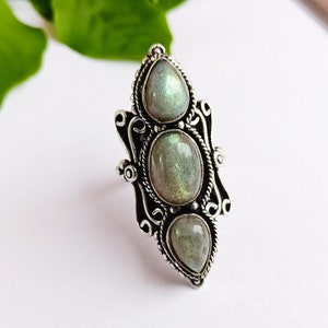 May include: A silver ring with three oval-shaped labradorite gemstones set in a decorative filigree design.
