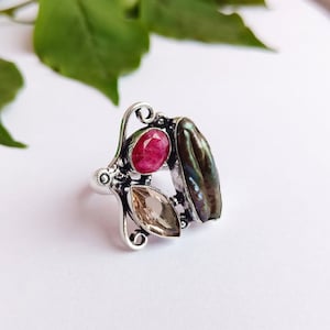 May include: A silver ring featuring a pink, brown, and green gemstone setting. The ring has a delicate, ornate design.