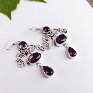 May include: A pair of silver earrings with purple gemstone accents. The earrings feature a delicate, ornate design with multiple stones.