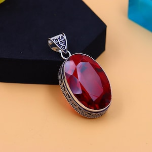 May include: A silver pendant featuring an oval red gemstone set within an intricate silver frame.