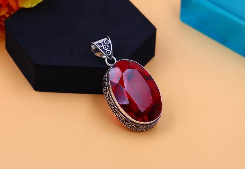 May include: A silver pendant featuring an oval red gemstone set within an intricate silver frame.