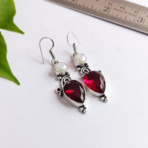 Könnte beinhalten: Ein Paar silberne Ohrhänger mit roten Edelstein-Tropfen und weißen Perlen-Akzenten.