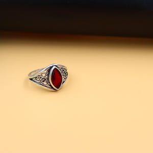 May include: A silver ring with a red gemstone set in a Celtic knot design.