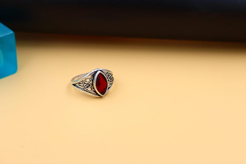 May include: A silver ring with a red gemstone set in a Celtic knot design.