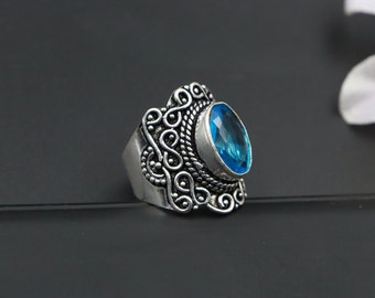 May include: A silver ring with an ornate design and a large, oval-shaped blue gemstone.