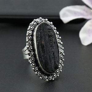 Puede incluir: Un anillo de plata con una piedra ovalada negra engastada en un engaste decorativo de plata. El anillo tiene un diseño detallado con pequeños círculos alrededor de la piedra.