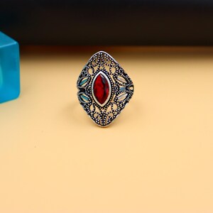 Op de afbeelding: Een zilveren ring met een rode edelsteen in een filigraan ontwerp.